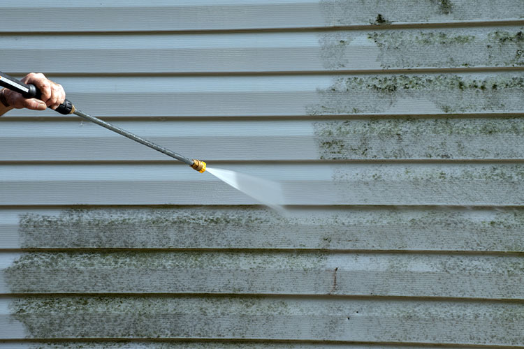 Someone power-washing the siding of a dirty home