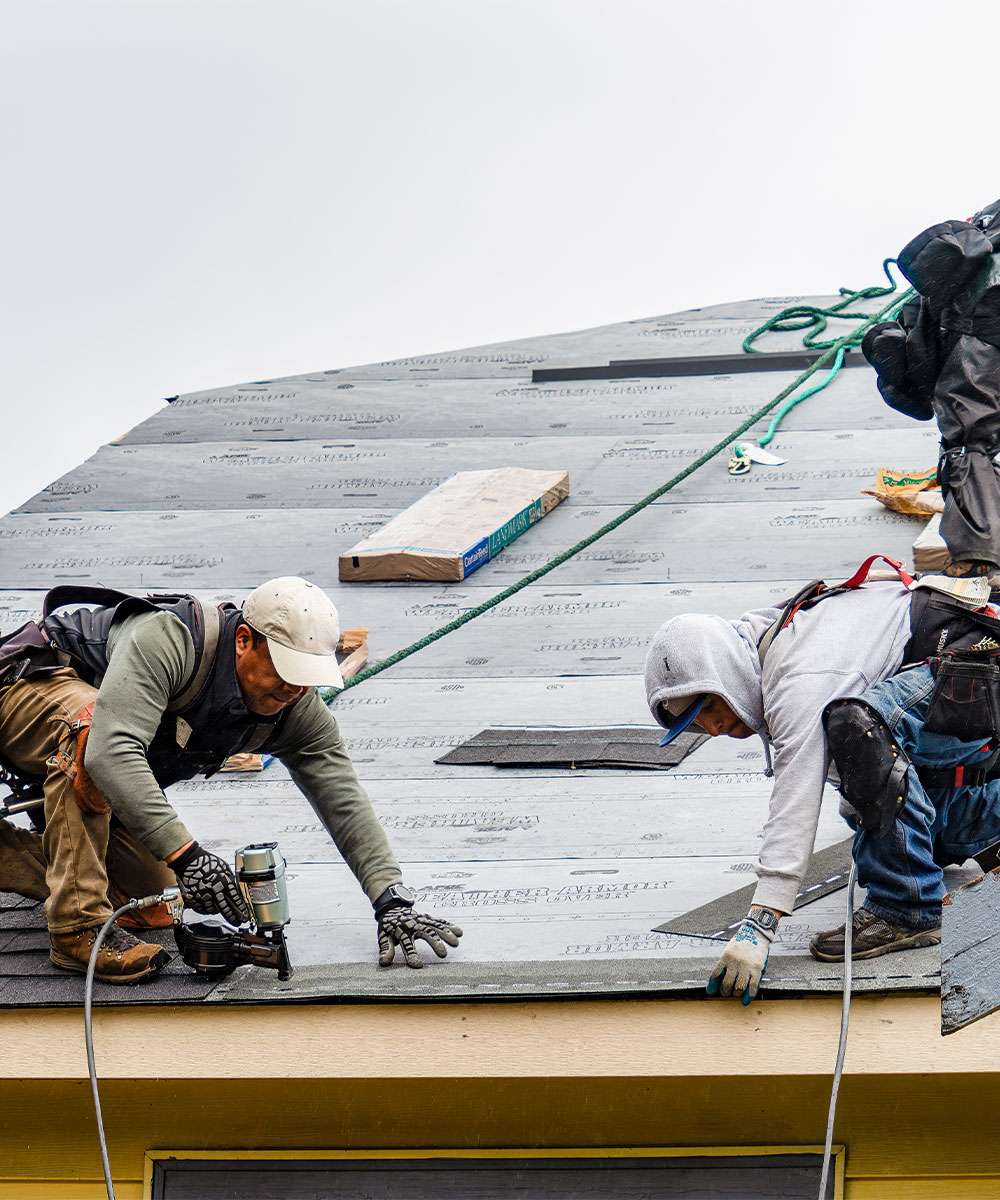 Three roofers working to nail the roll roofing to a roof